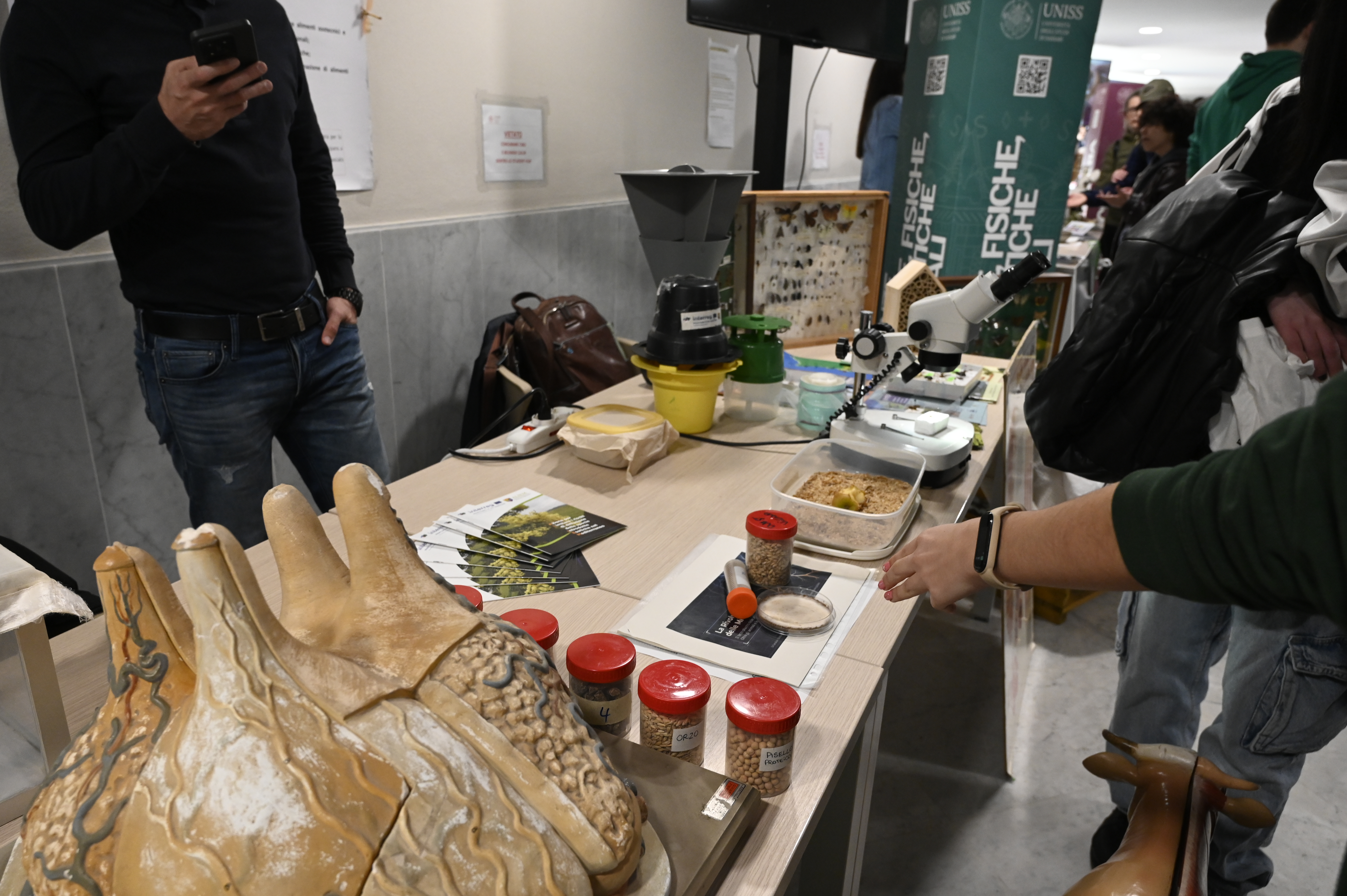 Stand scientifico UNISS con microscopio, modelli didattici e materiali divulgativi, durante una giornata di orientamento dedicata agli studenti