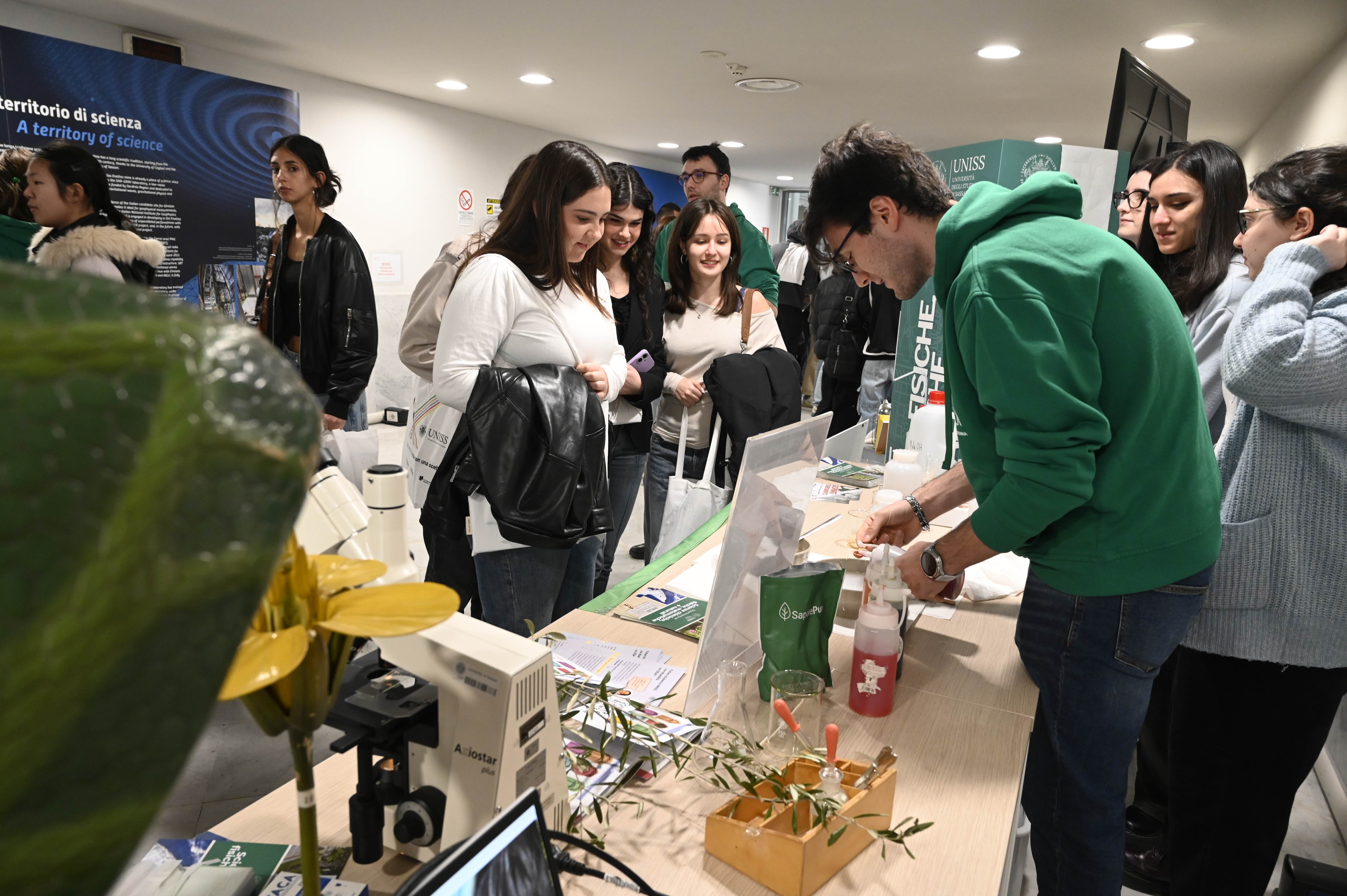 Attività dimostrativa presso uno stand universitario UNISS, con studenti coinvolti in un laboratorio interattivo e osservazioni scientifiche
