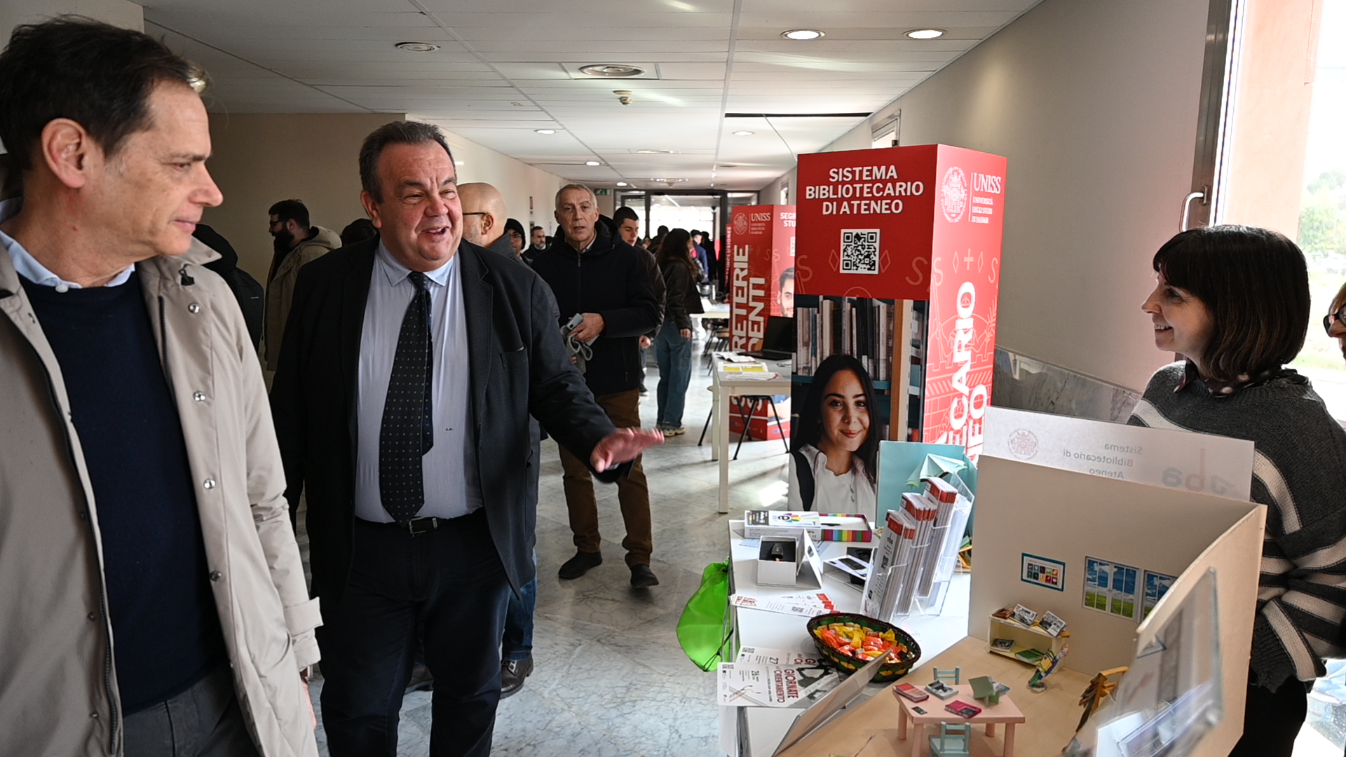 Stand scientifico UNISS con microscopio, modelli didattici e materiali divulgativi, durante una giornata di orientamento dedicata agli studenti.