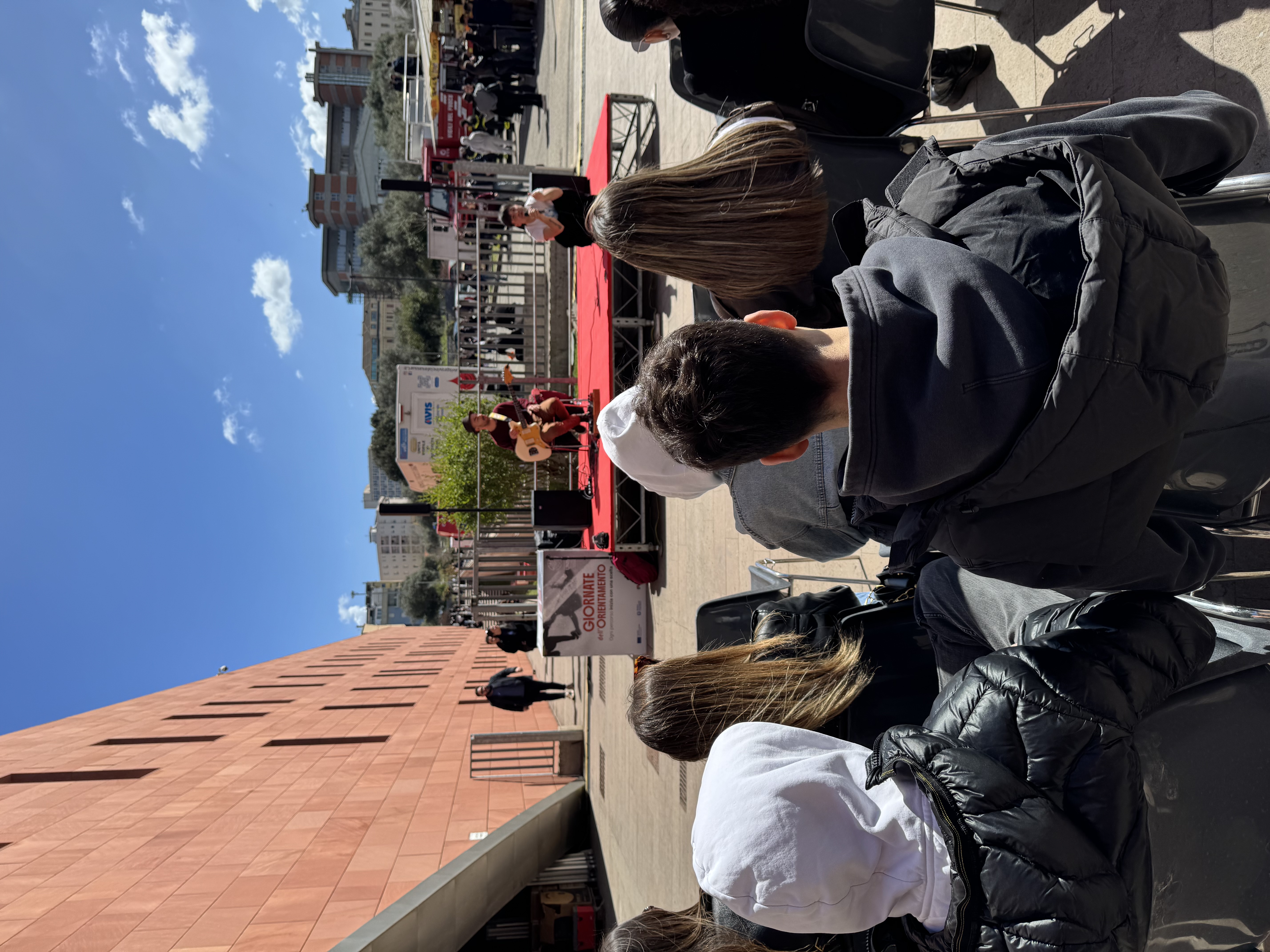 Performance musicale dal vivo all’aperto durante un evento UNISS, con pubblico seduto e palco allestito negli spazi esterni del campus