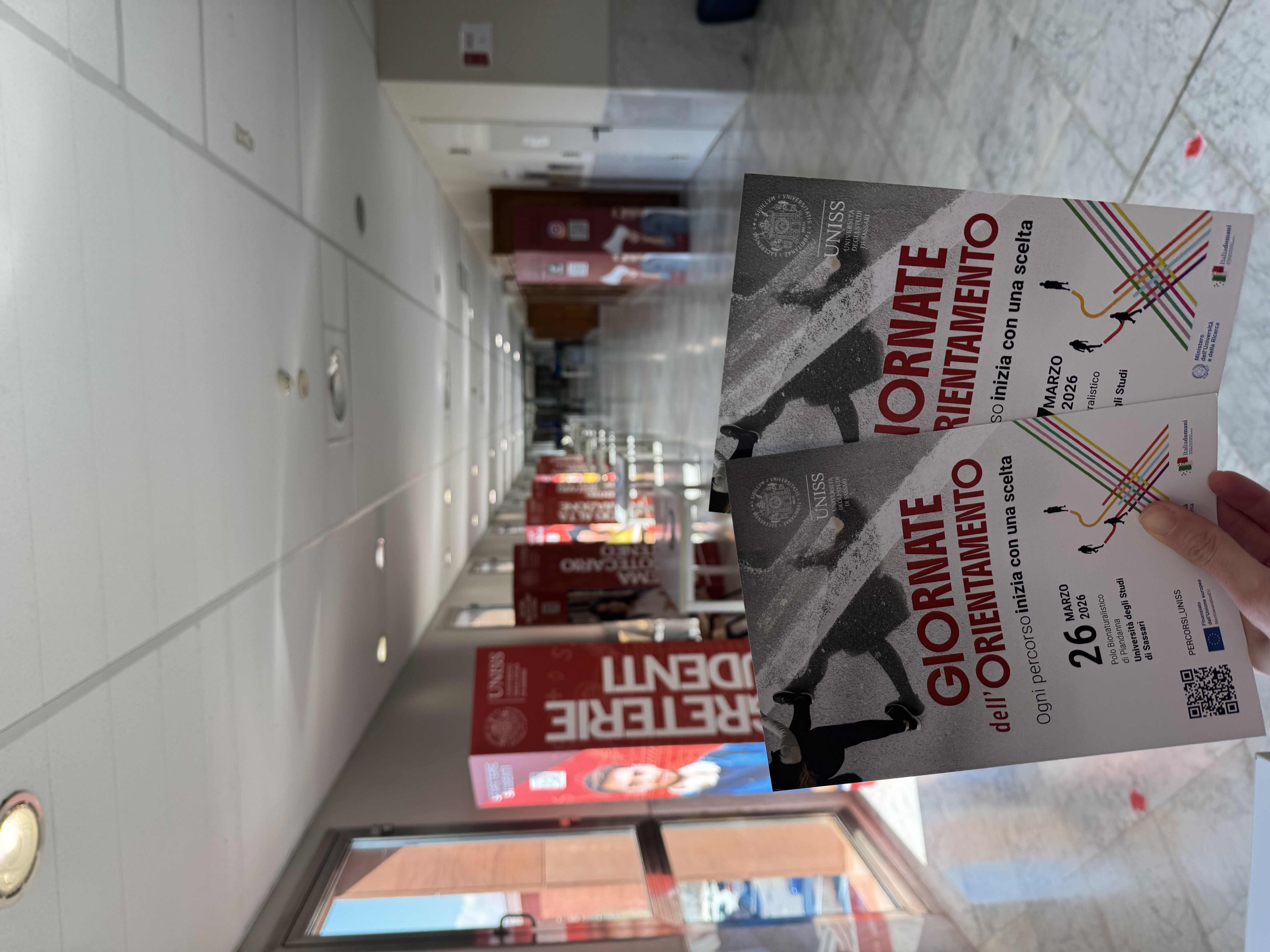 Volantini delle Giornate dell’Orientamento UNISS in primo piano all’interno del polo universitario, con corridoio allestito per l’accoglienza