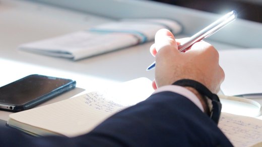 Braccio appoggiato al banco che impugnando una penna scrive su quaderno